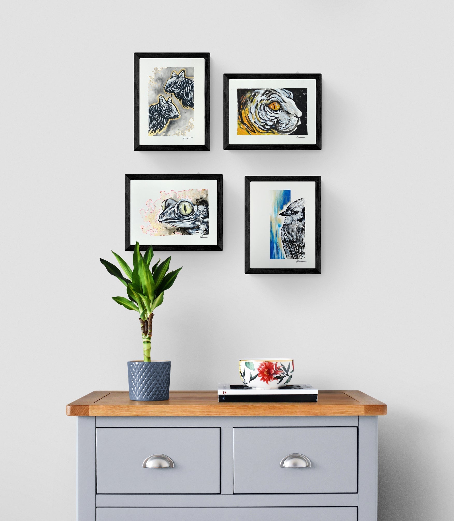 4 oeuvres encadrées représentant des écureils, un chat, une grenouille et un geai bleu accroche au mur au dessus d'une commode grise